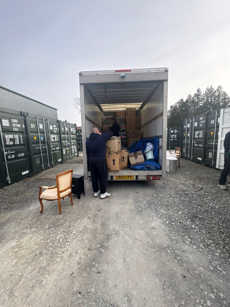 New Moves team loading boxes and a wooden chair from a storage unit into the back of a removal van