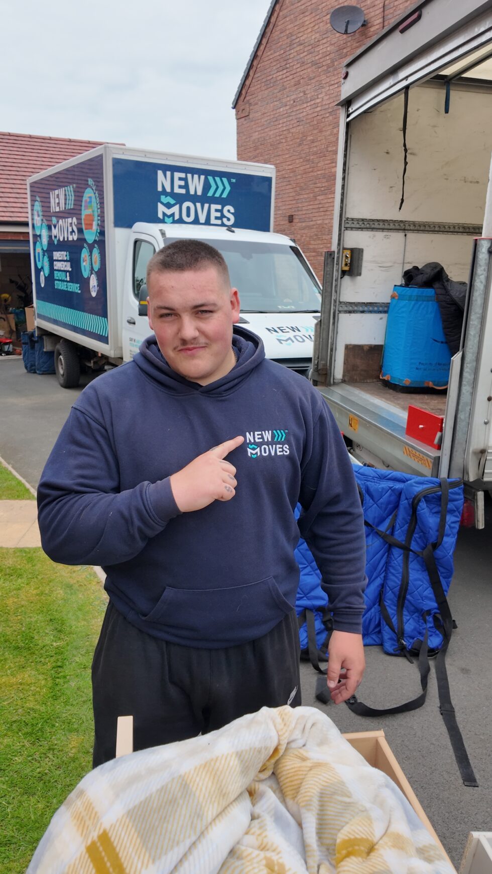 New Moves team member pointing to the logo on his branded hoodie while loading blankets and packing materials into a removal van