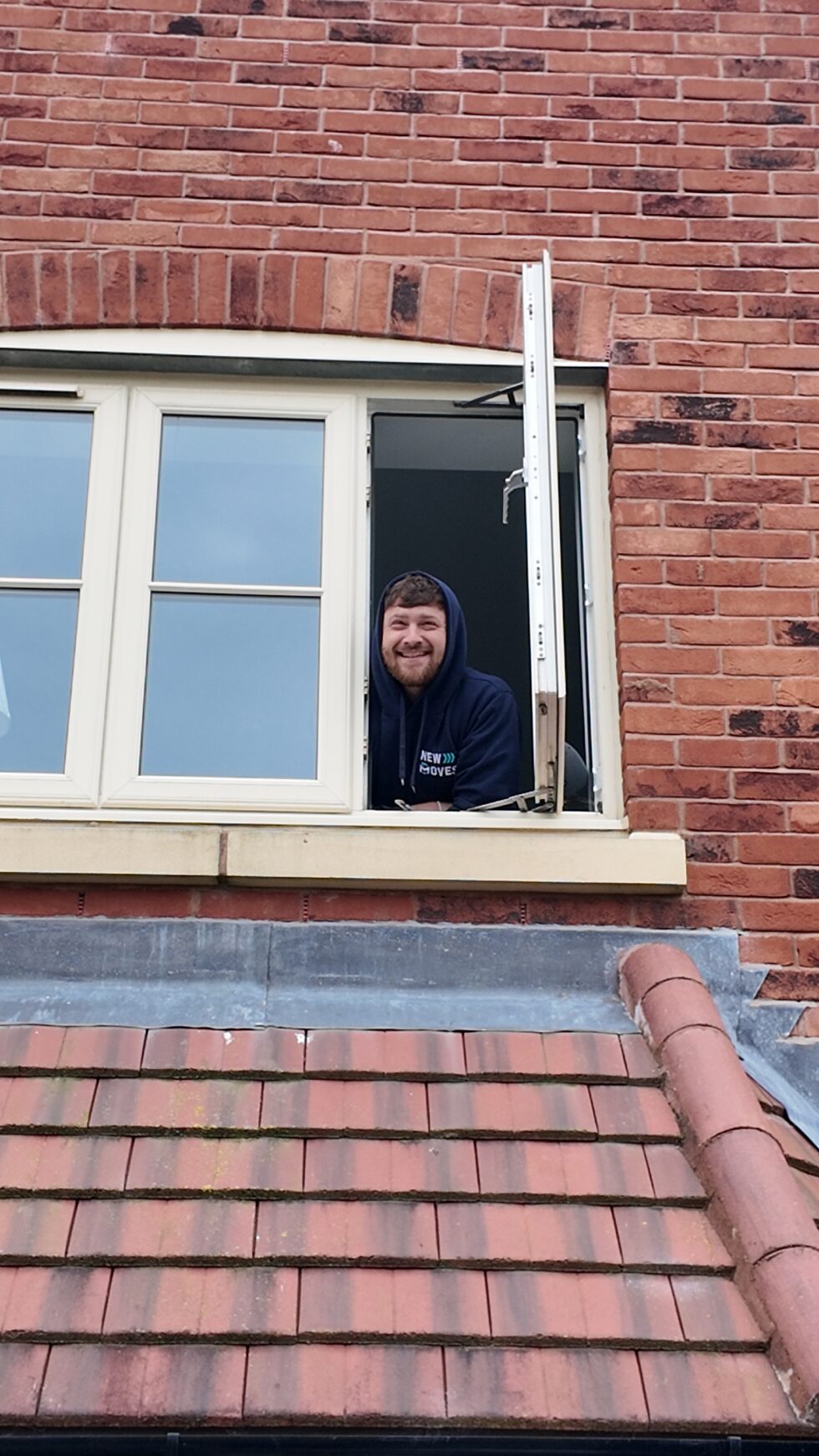New Moves team member smiling and leaning out of an upstairs window of a brick house being worked on during a move