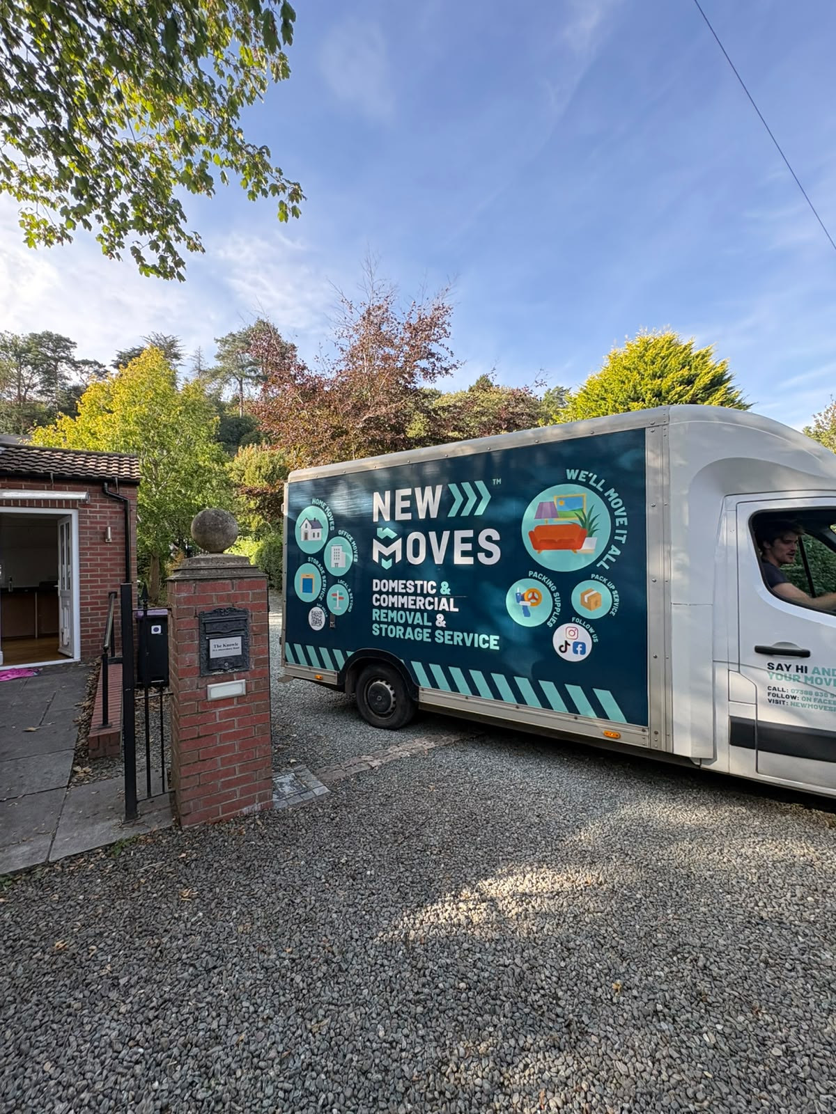 A New Moves Removals van parked on a gravel driveway beside a stone gate pillar