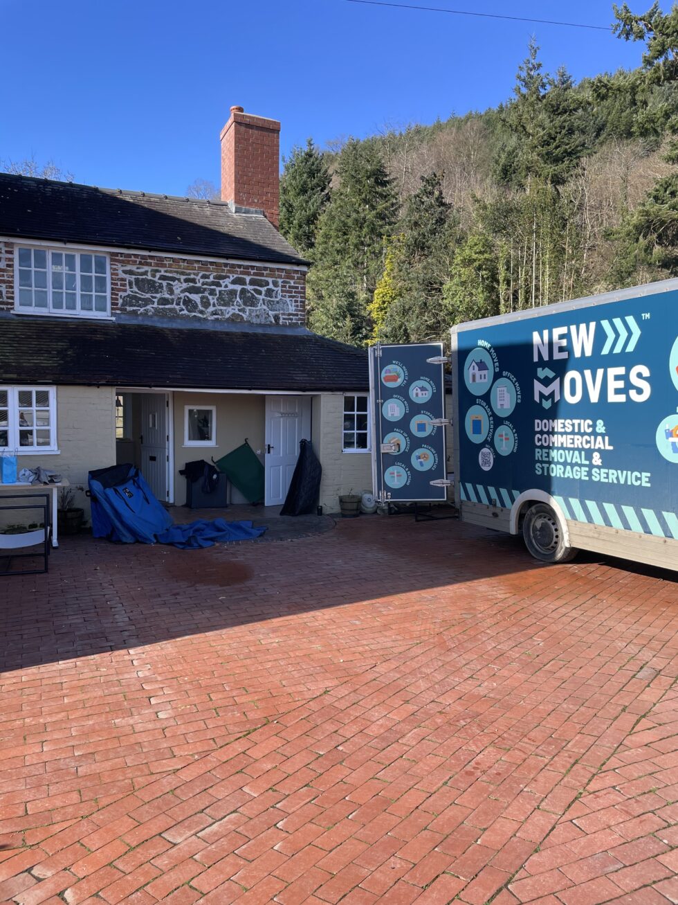 A New Moves Removals van backed up to the front door of a stone cottage, with wrapped furniture ready to load